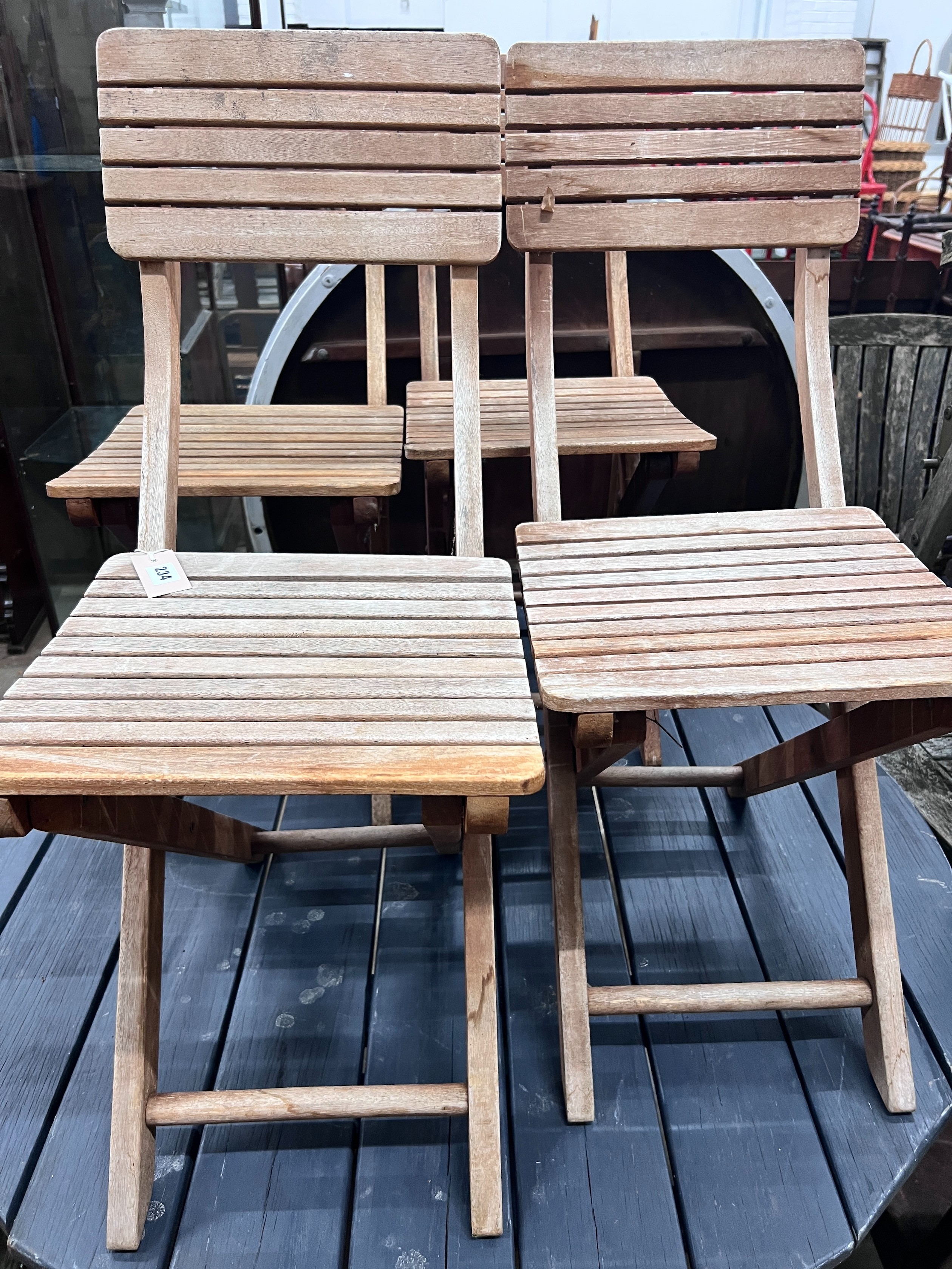 A grey stained teak circular garden table and four faded teak folding chairs, table diameter 120cm